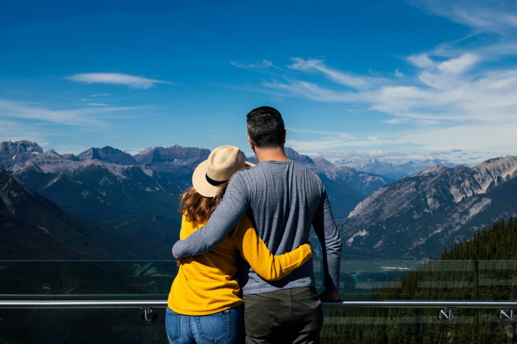 Couple embracing while looking out over a scenic mountain range under a clear blue sky, symbolising financial freedom, long-term planning, and peace of mind.